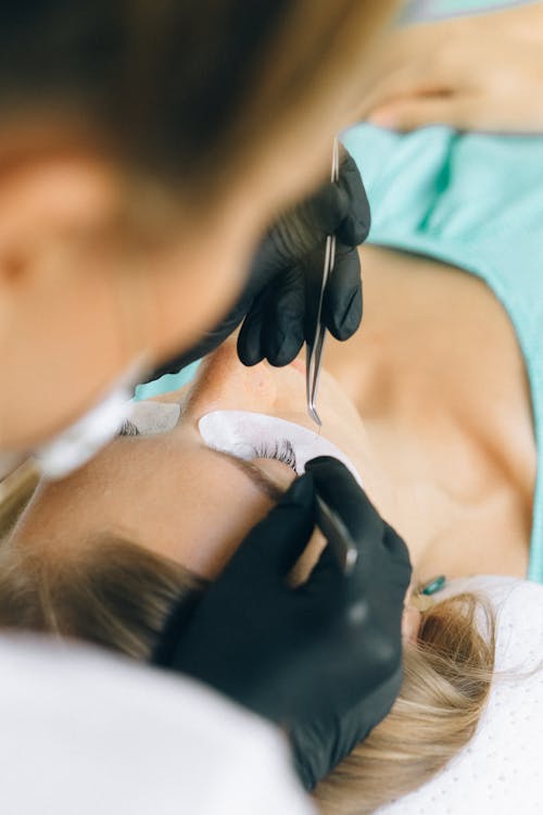Technicienne en gants posant des extensions de cils, choisir entre rehaussement et extensions